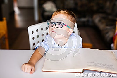 Cute toddler boy with down syndrome with big glasses reading intesting book Stock Photo