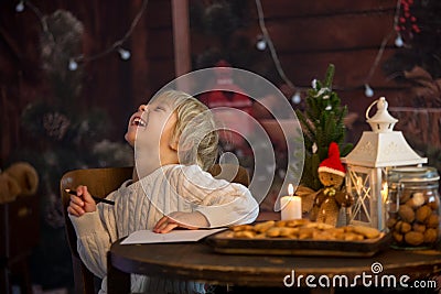 Cute toddler child, boy on Christmas, writing letter to Santa Claus and eating cookies at home, wooden cottage Stock Photo