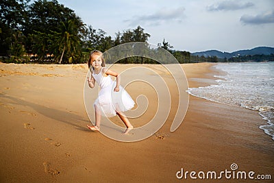 Cute toddler girl with blonde hair in a white tutu dress running on a sandy beach at sunset. Happy childhood memories Stock Photo