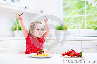 Cute toddler girl eating spaghetti in a white kitchen Stock Photo