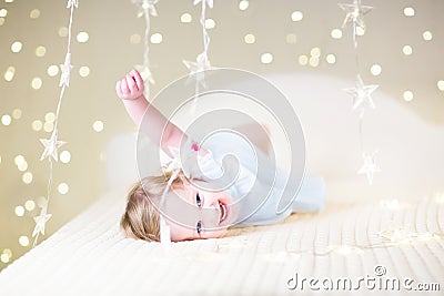 Cute toddler girl playing on a bed between warm soft Christmas l Stock Photo