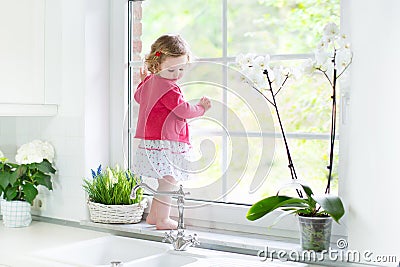 Cute toddler girl watching out window in white kitchen Stock Photo