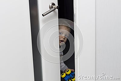 Cute toddler looking out from behind the ajar door Stock Photo