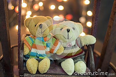 Cute two doll bears. Pair of cute teddies are sitting on wood swing with bokeh light in background. Teddies wear winter suite. Hug Stock Photo