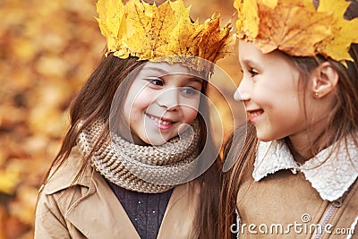 Cute two little sisters with crown of leaves hugging in autumn park Stock Photo