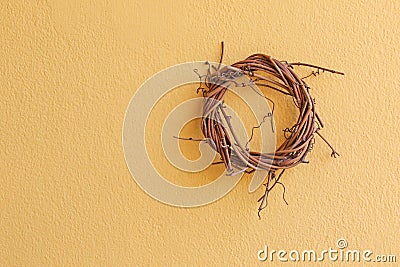 Cute wicker wooden wreath made of dried branch hanging on yellow Stock Photo