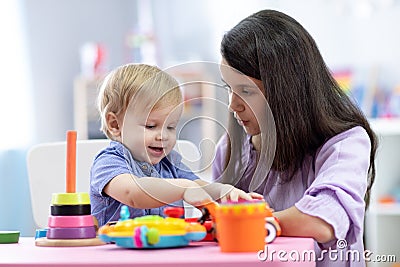 Cute woman with child playing with plastic blocks at home or kindergarten Stock Photo