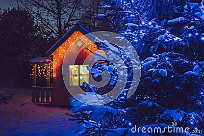 Cute wood play house in home garden, decorated with Christmas LED string lights outdoors. Stock Photo