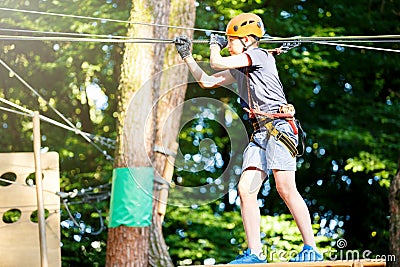 Cute young boy in helmet with climbing equipment in the rope amusement park. Summer camp, holidays Stock Photo