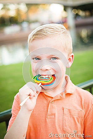 Cute young boy licking a large colorful lollipop outdoors Stock Photo