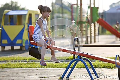Cute young child girl outdoors on see-saw swing on sunny summer day Stock Photo
