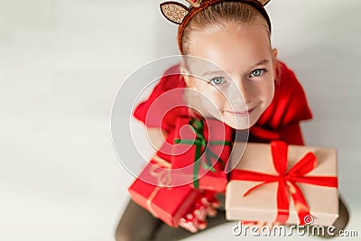 Cute young girl holding christmas presents, smiling and looking at camera. Happy kid at christmas time sitting on the floor. Stock Photo