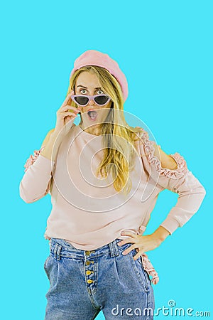 Cute young girl in jeans, sweater, pink birete and glasses, lowered glasses from eyes with delight on the face, emotions Stock Photo