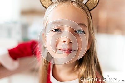 Cute young girl wearing costume reindeer antlers, smiling and looking at camera. Happy kid at christmas. Stock Photo