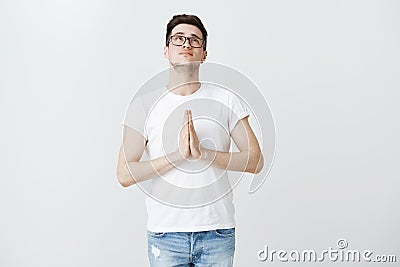 Cute young guy feeling upbeat asking god help pass interview. Charming hopeful male in glasses holding hands in pray Stock Photo