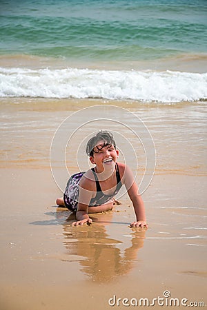 Cute young little girl laughing laying in a swimsuit in the sand on a beach. Stock Photo