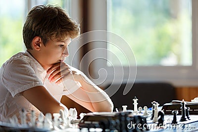 Cute young smart boy in plays chess on the training before the tournament. Hand makes a move on chessboard. Chess summer camp. Stock Photo