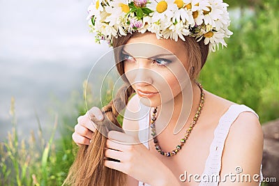 Cute young woman with circlet of camomile braiding her hair at t Stock Photo