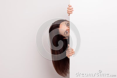 Cute young woman with long hair peering around from behind white Stock Photo