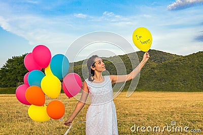 Cute young woman in white dress with balloons in her hands. The concept of freedom and joy. Balloon with text in the left hand Stock Photo