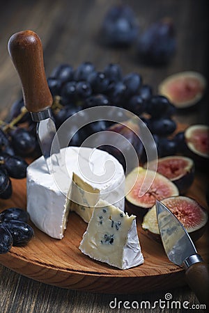 Cuted blue cheese, fresh fig halfs and grapes on rustic wooden plate. Moody scene with selective focus Stock Photo