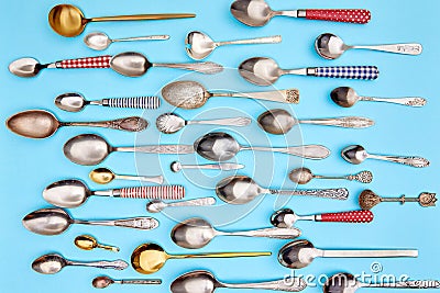 Cutlery. Flat lay photo of variety of antique silverware and gold kitchen spoons arranged against blue studio background Stock Photo