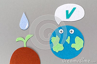 Cutted out of felt the planet Earth with emoticon and soil with a watered plant sprout. Gray background. Flat lay. Earth Day Stock Photo