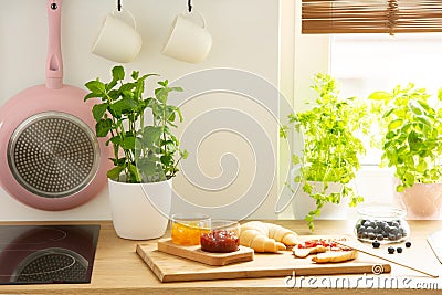 Cutting board with French croissants and fruit jams and natural herbs in a bright kitchen interior with a white wall Stock Photo