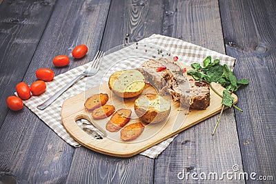 On a cutting board, slices of baked meat, baked potatoes and car Stock Photo