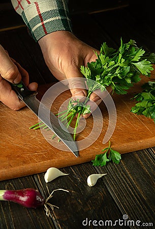 Cutting parsley with a knife on a cutting board. Cooking vegetable salad in the kitchen by the hands of a cook. The idea of a Stock Photo