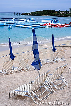 Cyan sea waves hitting sandy beach with dark blue closed umbrellas and sunbeds on aqua park Stock Photo
