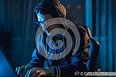 Cybercriminal hacker in the hood typing program code while stealing access databases with passwords. Cyber security Stock Photo