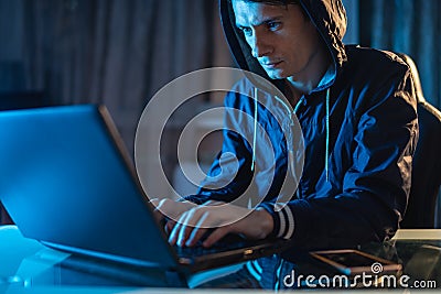 Cybercriminal hacker in the hood typing program code while stealing access databases with passwords. Cyber security Stock Photo