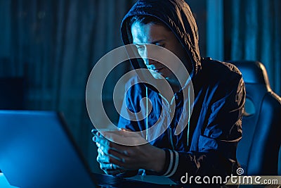 Cybercriminal hacker in the hood typing program code while stealing access databases with passwords. Cyber security Stock Photo