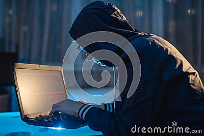 Cybercriminal in the hood typing program code while stealing access databases with passwords. Hackers and cyber security Stock Photo