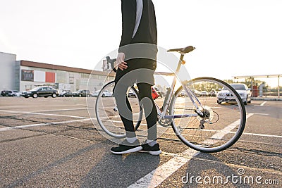 Cyclist in dark sportswear with a highway bike on the background of parking in the sunset Stock Photo
