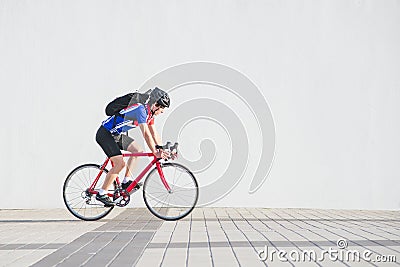 Cyclist in a helmet, athletic cycling clothes and a backpack rides on the background of a white wall Stock Photo