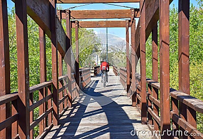 cyclist with helmet riding his mountain bike crossing a wooden brown bridge in a sunny day. Rider wears a red sweeter. Horizontal Editorial Stock Photo