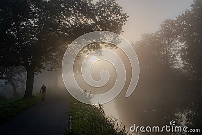Cyclist on a Misty Riverside Journey at Dawn Stock Photo