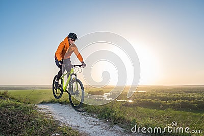 A cyclist in an orange hoodie rides a bike along a mountain path. The concept of extreme sports. Stock Photo