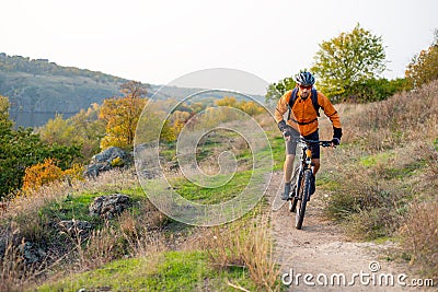 Cyclist in Orange Riding the Mountain Bike on the Autumn Rocky Trail. Extreme Sport and Enduro Biking Concept. Stock Photo