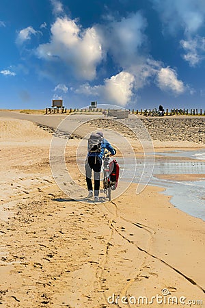 Cyclist pushing a trekking bike on a sandy beach, traveling by bicycle on the coast on vacation. Stock Photo