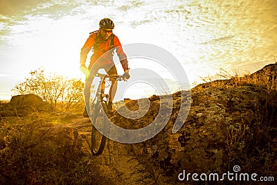 Cyclist in Red Riding the Bike on Autumn Rocky Trail at Sunset. Extreme Sport and Enduro Biking Concept. Stock Photo