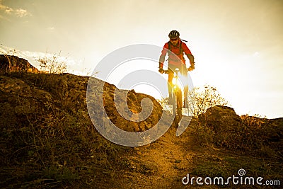 Cyclist in Red Riding the Bike on Autumn Rocky Trail at Sunset. Extreme Sport and Enduro Biking Concept. Stock Photo