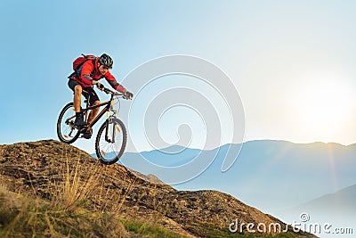 Cyclist in Red Riding the Bike Down the Rock at Sunrise. Extreme Sport and Enduro Biking Concept. Stock Photo