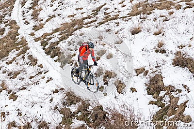Cyclist in Red Riding Mountain Bike on the Snowy Trail. Extreme Winter Sport and Enduro Biking Concept. Stock Photo