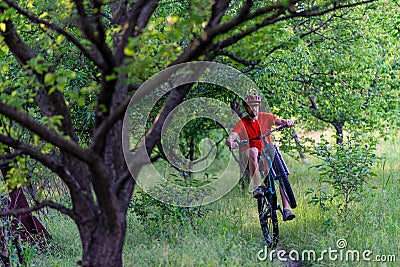 A cyclist rides on the rear wheel of a bicycle along a forest path. Active lifestyle, extreme Stock Photo