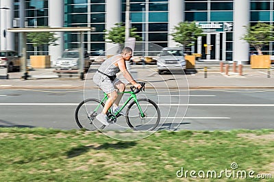 Cyclist riding a bicycle on the city street. Amateur cyclist in gray cycling garment rushing bicycle outdoors on a sunny day Editorial Stock Photo
