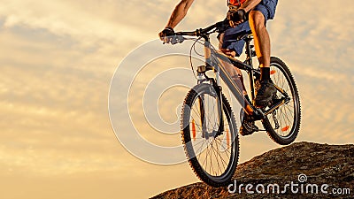 Cyclist Riding the Bike Down the Rock at Sunset. Extreme Sport and Enduro Biking Concept. Stock Photo