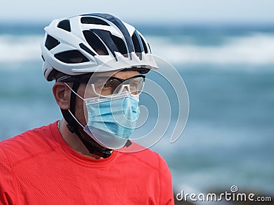 Cyclist sportsman wears protective face mask and white bike helmet on blue ocean. Stock Photo